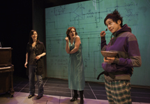 3 women stand discussing in front of a giant circuit diagram