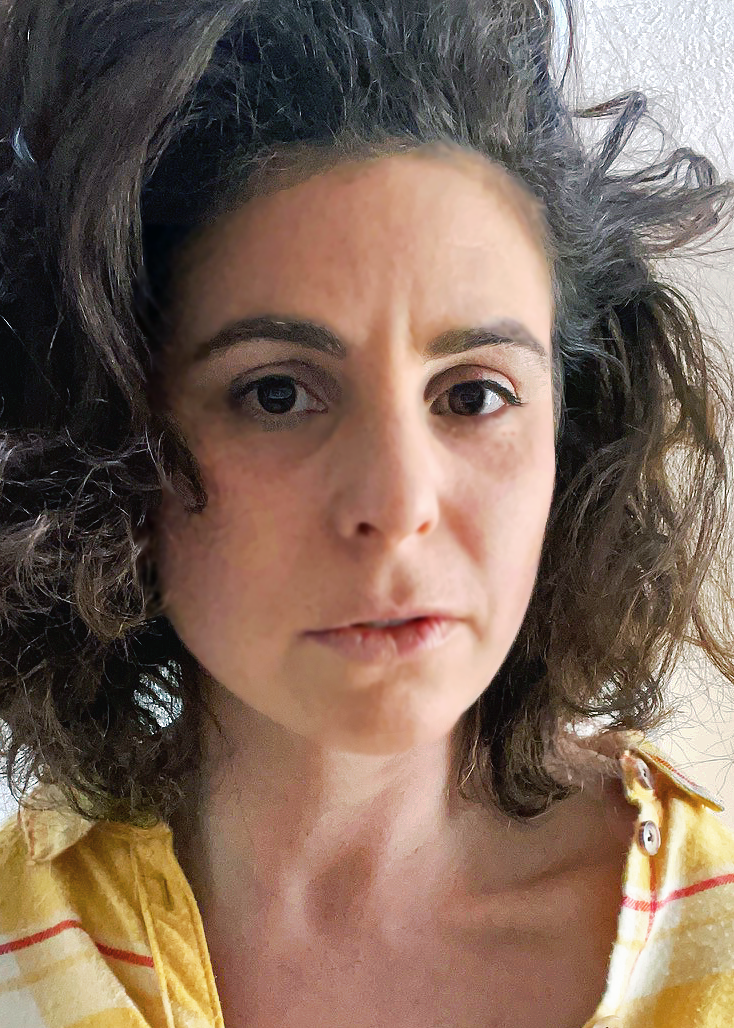 Rachel faces the camera in a close-up portrait. She has dark, curly shoulder-length hair and a calm, neutral expression. She wears a yellow top with thin red stripes, photographed in soft light against a pale background.