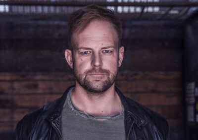 Under a head of sandy coloured hair which gives the illusion of “I just woke up like this” but also took far too long to perfect, is a scruffy face, hopefully not quite showing my age. My face has a not so subtle mix of freckles and dots and hosts a sly grin that implies I know more about what’s going on than I probably do. This sly grin is second to my most defining characteristic. My left eye a deep ocean blue and my right a jet-black fading into midnight. I am wearing a thin, green sweater with minor and very fashionable rips that, yes, I did myself, under a black leather jacket.